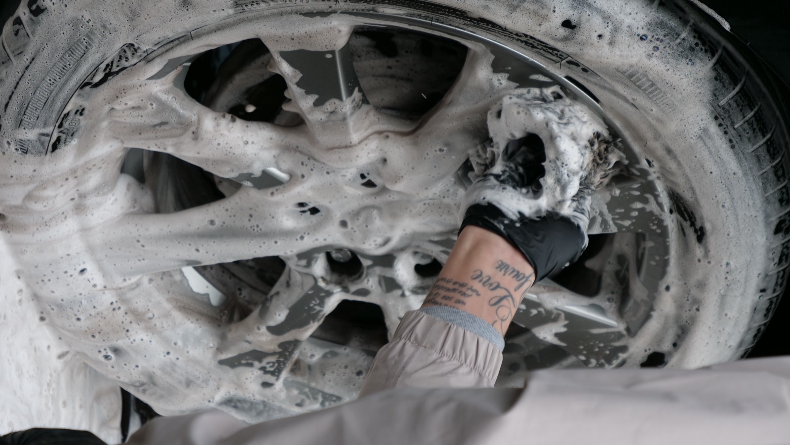 Gloved hand foaming and cleaning an alloy wheel